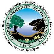 The image is a logo for the Cambria Community Services District, featuring a tree, ocean, and mountainous scene. Established in 1976.