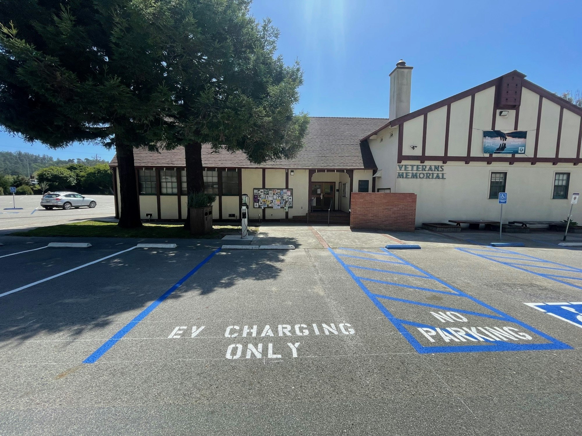 Electric vehicle charging station with designated parking in front of a Veterans Memorial building under clear skies.