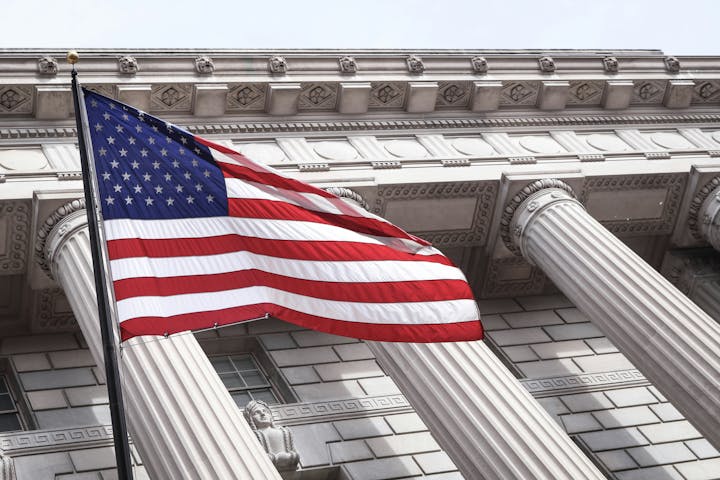 American flag waving in front of a neoclassical building with large columns.