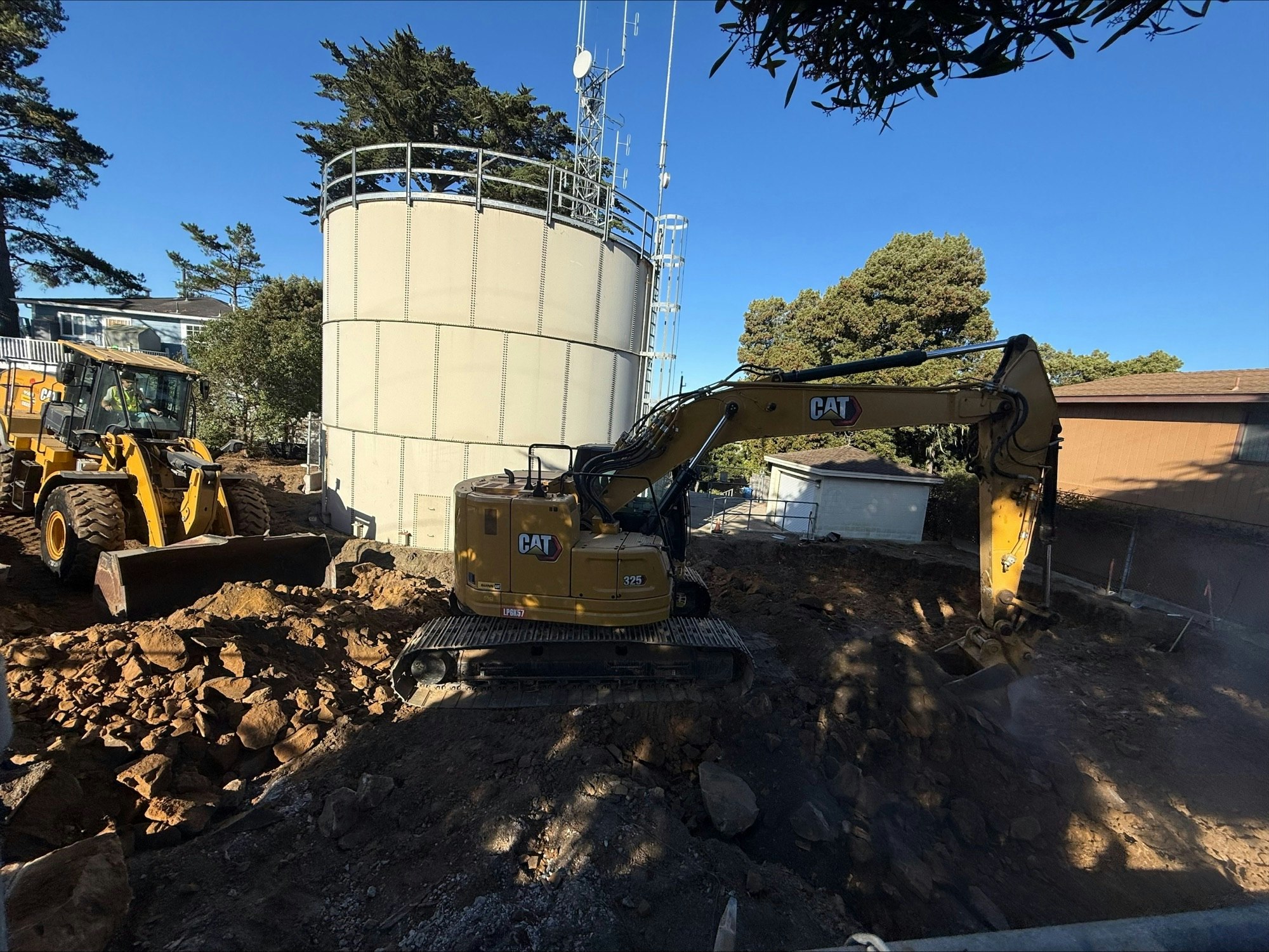 Construction site with two CAT machines, dirt, rocks, and a large cylindrical structure in the background.