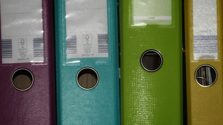 Four colored ring binders (purple, blue, green, yellow), standing side by side.