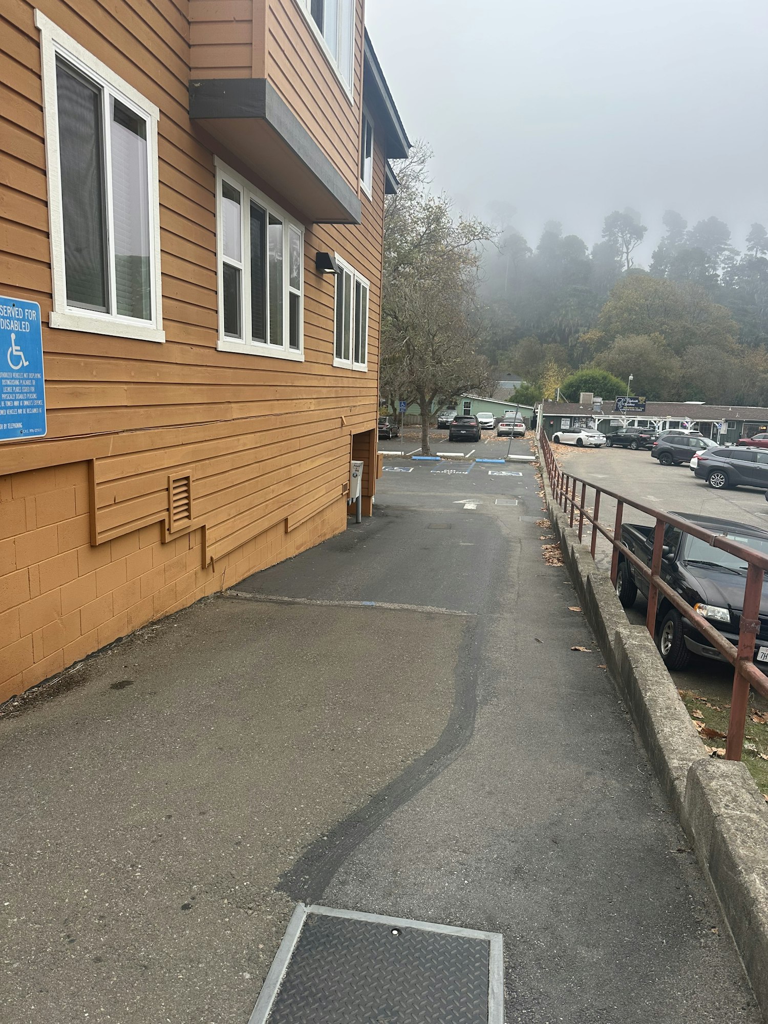 A foggy parking lot with cars, a wooden building, a ramp, and visible accessible parking signs.