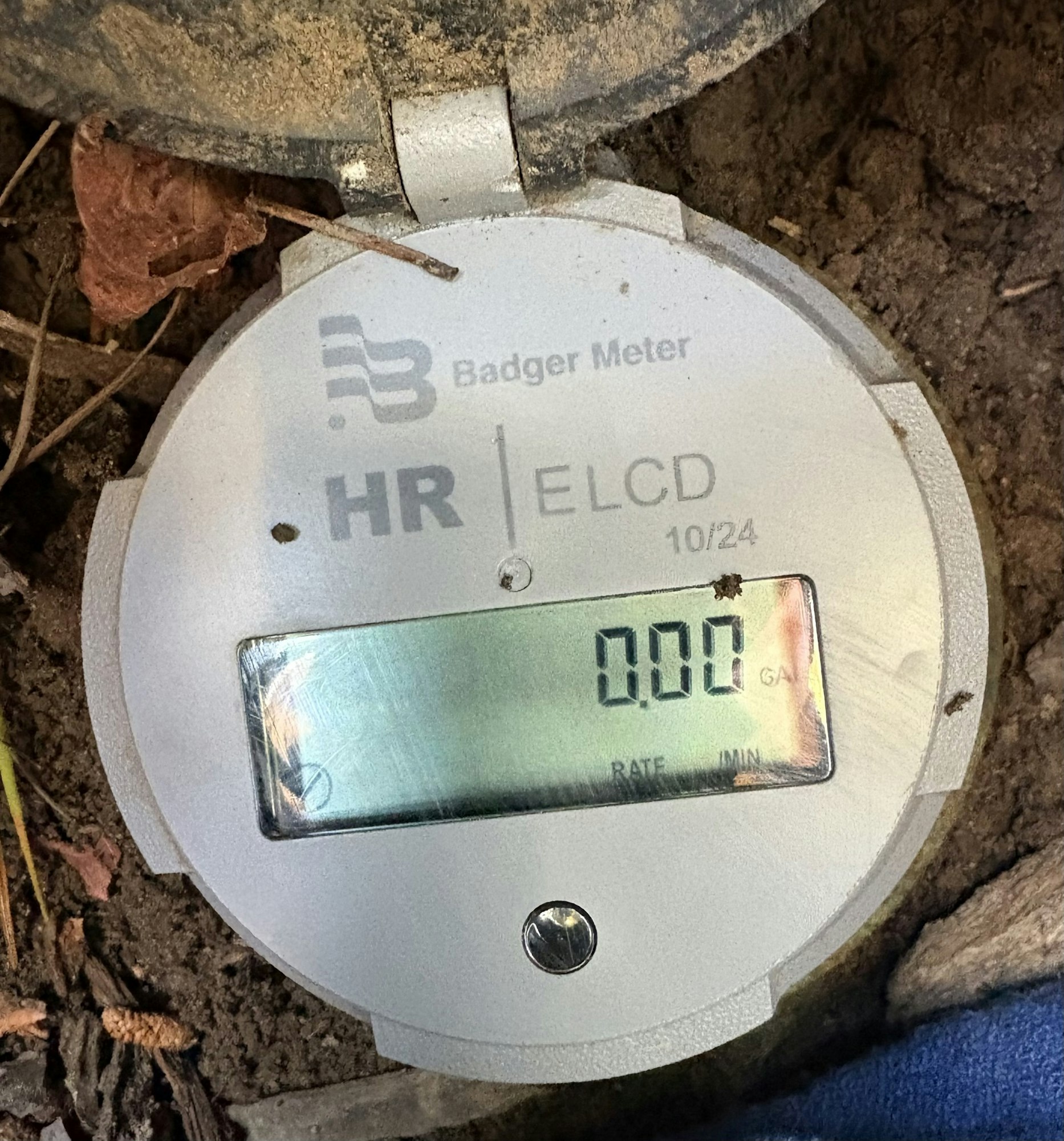 A digital water meter display by Badger Meter, showing "0.00" readings, partially covered in dirt.