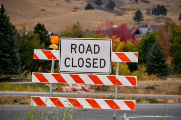 Road closed sign with orange and white barricades in a rural area.