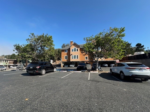 A parking lot with cars and a multi-story building in the background under a clear blue sky.