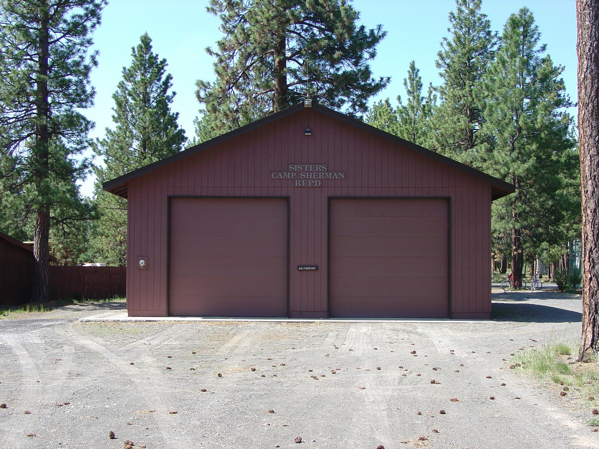 A brown building marked "Sisters Camp Sherman RFPD" with two garage doors, surrounded by pine trees.