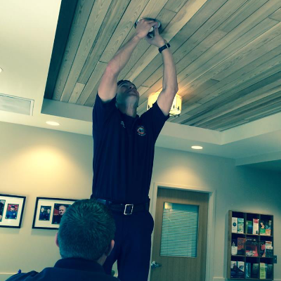 A person standing on a chair, reaching up to adjust a light fixture on a wooden ceiling. Another person watches nearby.