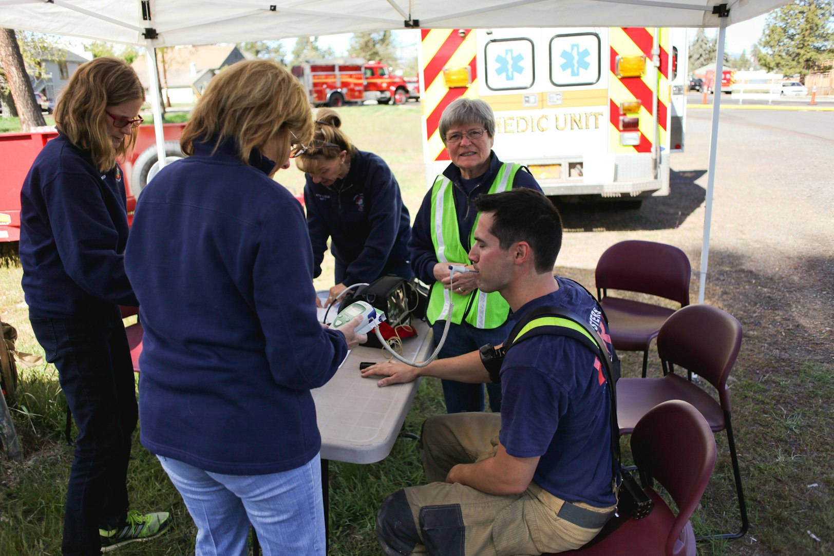 People gathered around a table under a tent, with medical equipment, likely involved in an emergency or training scenario.