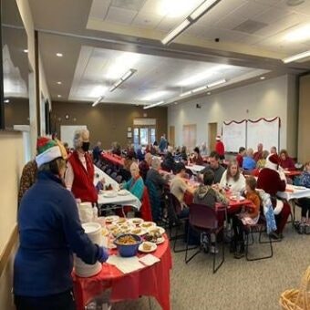 People sitting at tables in a community hall with a buffet table, possibly a holiday gathering.