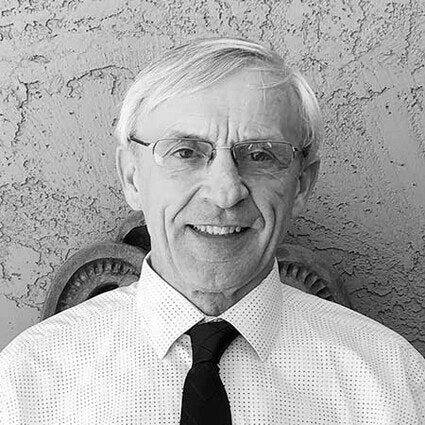 An older man with glasses and a tie, smiling in a black and white photo.