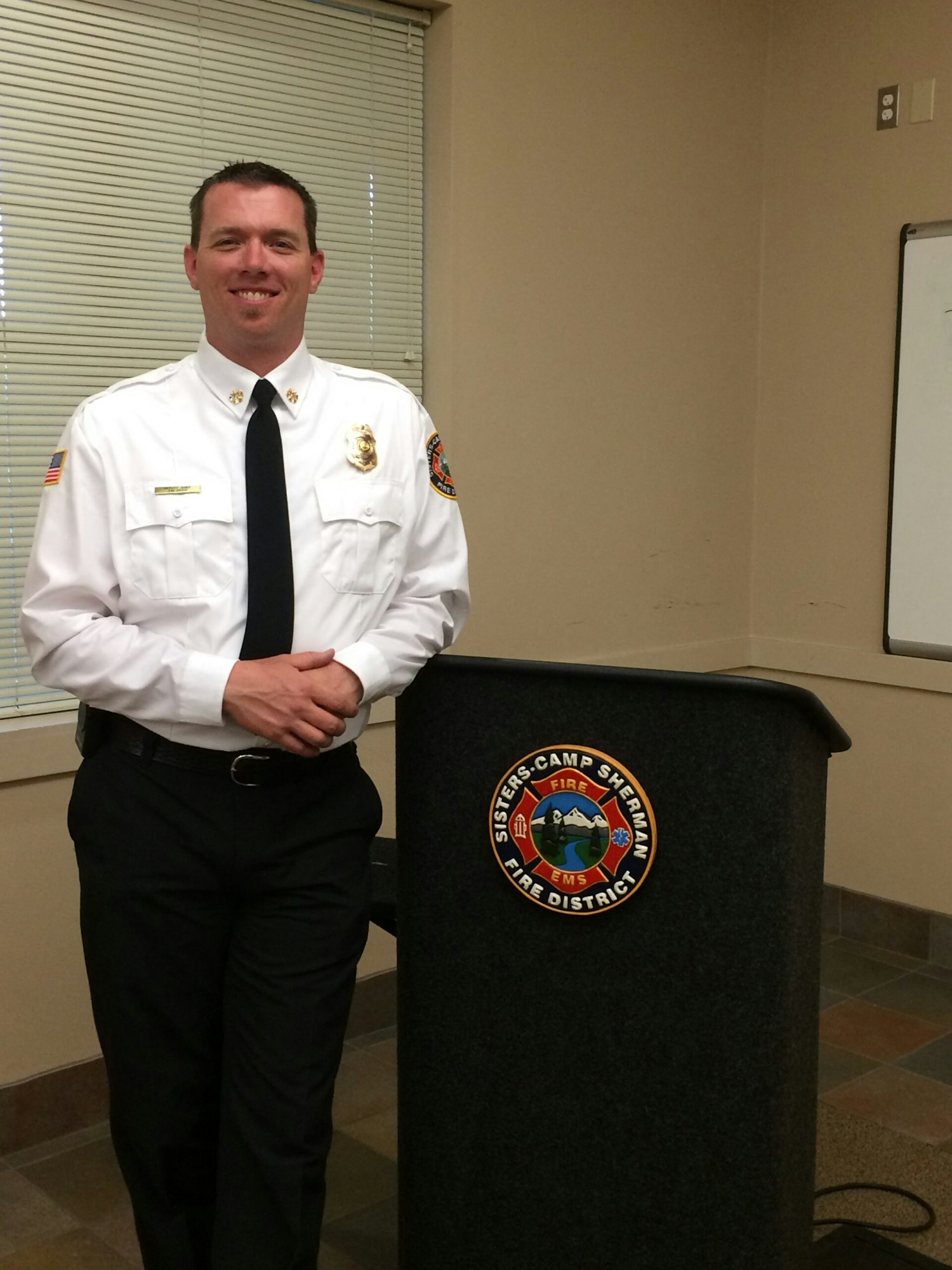 A person in a fire department uniform stands by a podium with the logo "Sisters-Camp Sherman Fire District."