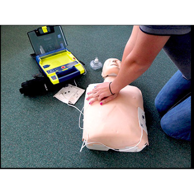 A person performs CPR on a practice dummy with an AED machine nearby.