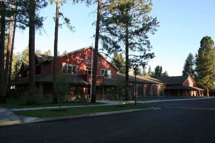 A red building surrounded by tall trees, with a sidewalk and road in the foreground under a clear sky.