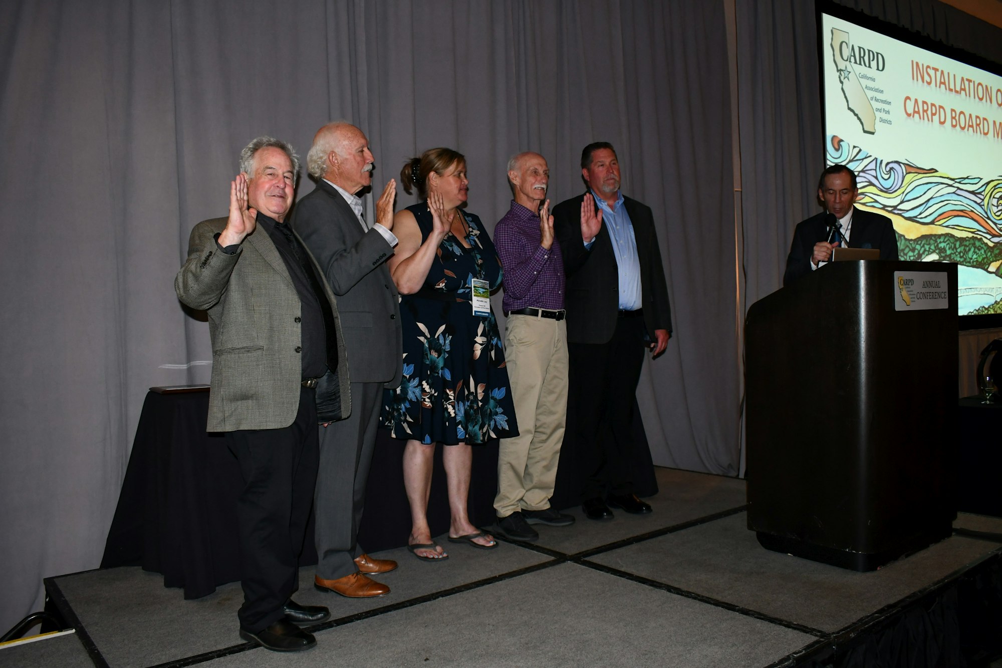 Group of people taking an oath at a conference, with one man speaking at a podium.