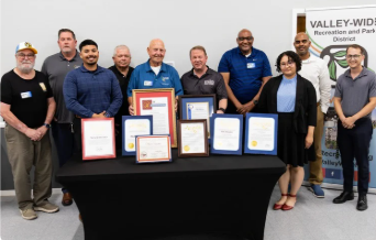A group of people stand behind a table displaying certificates and awards, with a "Valley-Wide Recreation and Park District" banner.