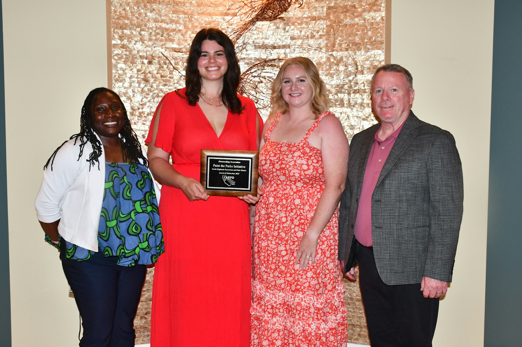 Four people posing, one holding an award plaque.