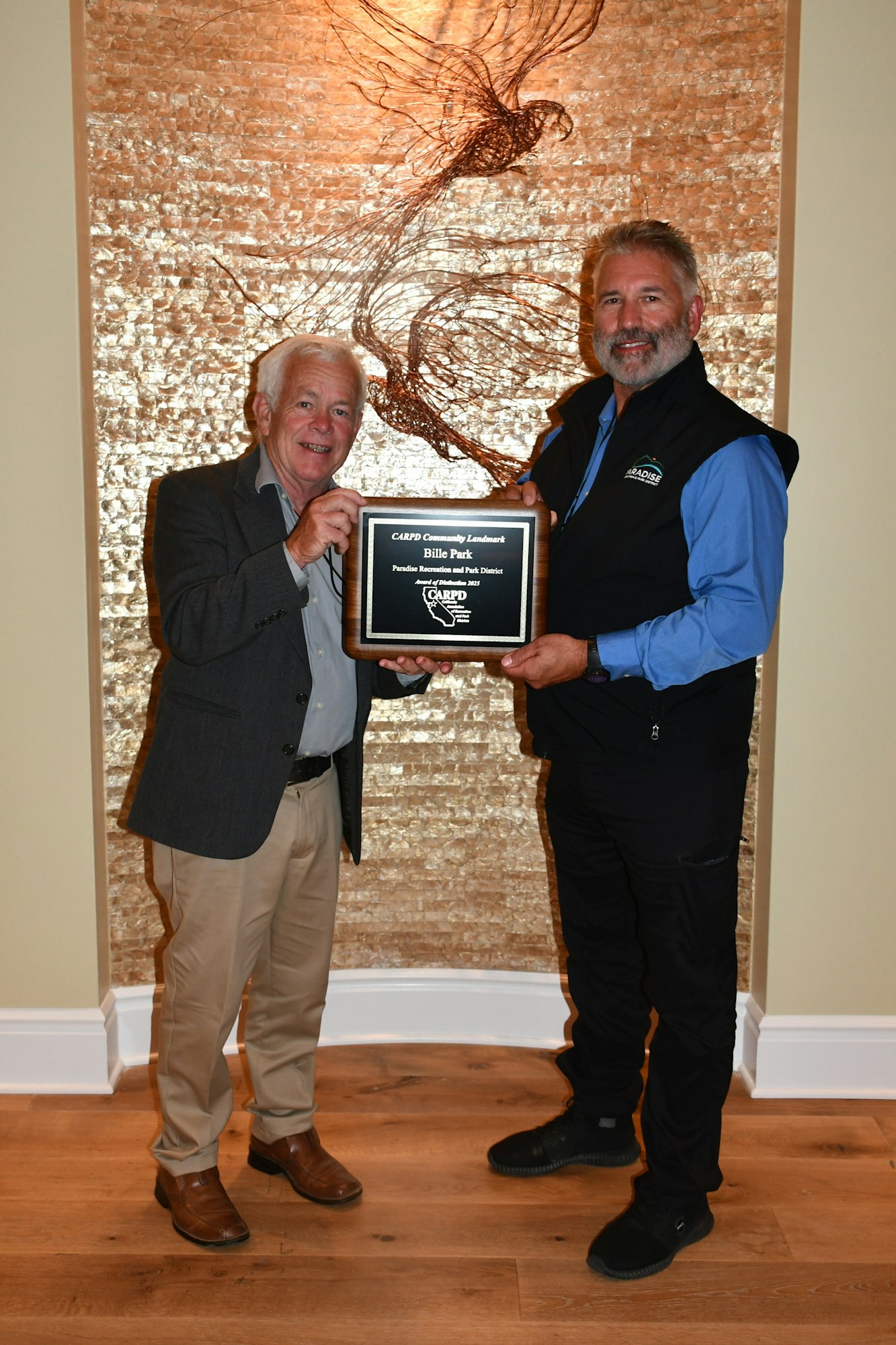 Two people holding a plaque in a decorated room with wooden flooring.