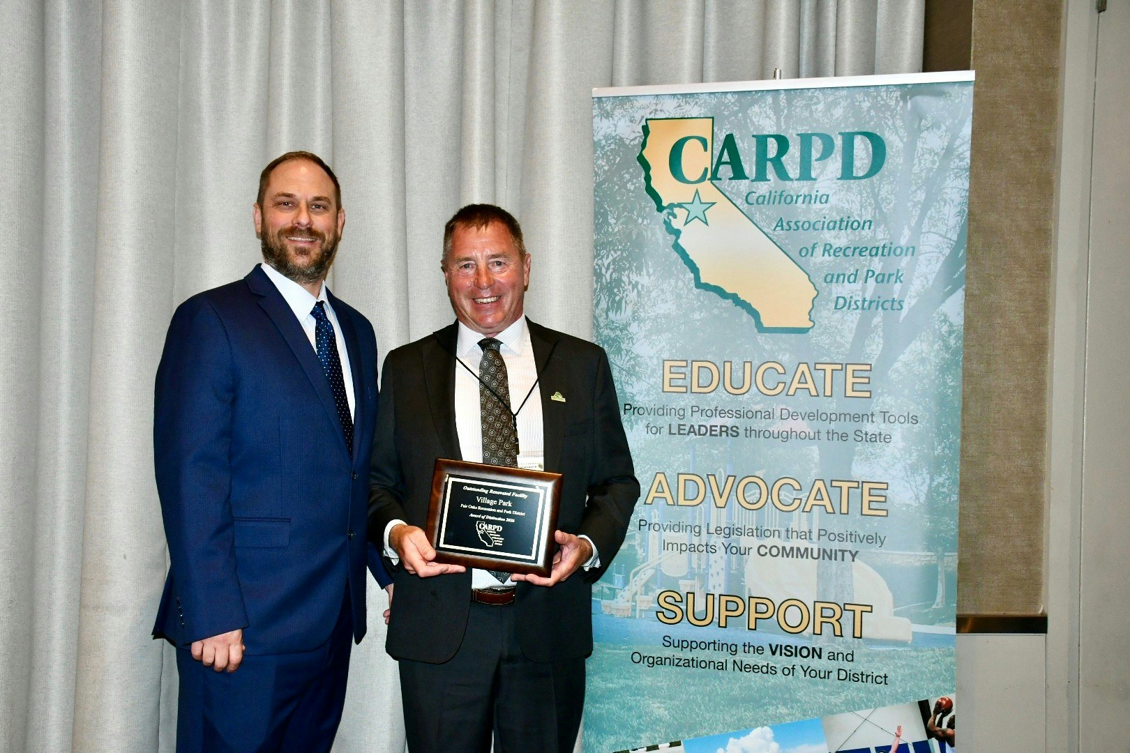 Two men are posing together, one holding an award, in front of a backdrop for the California Association of Recreation and Park Districts.