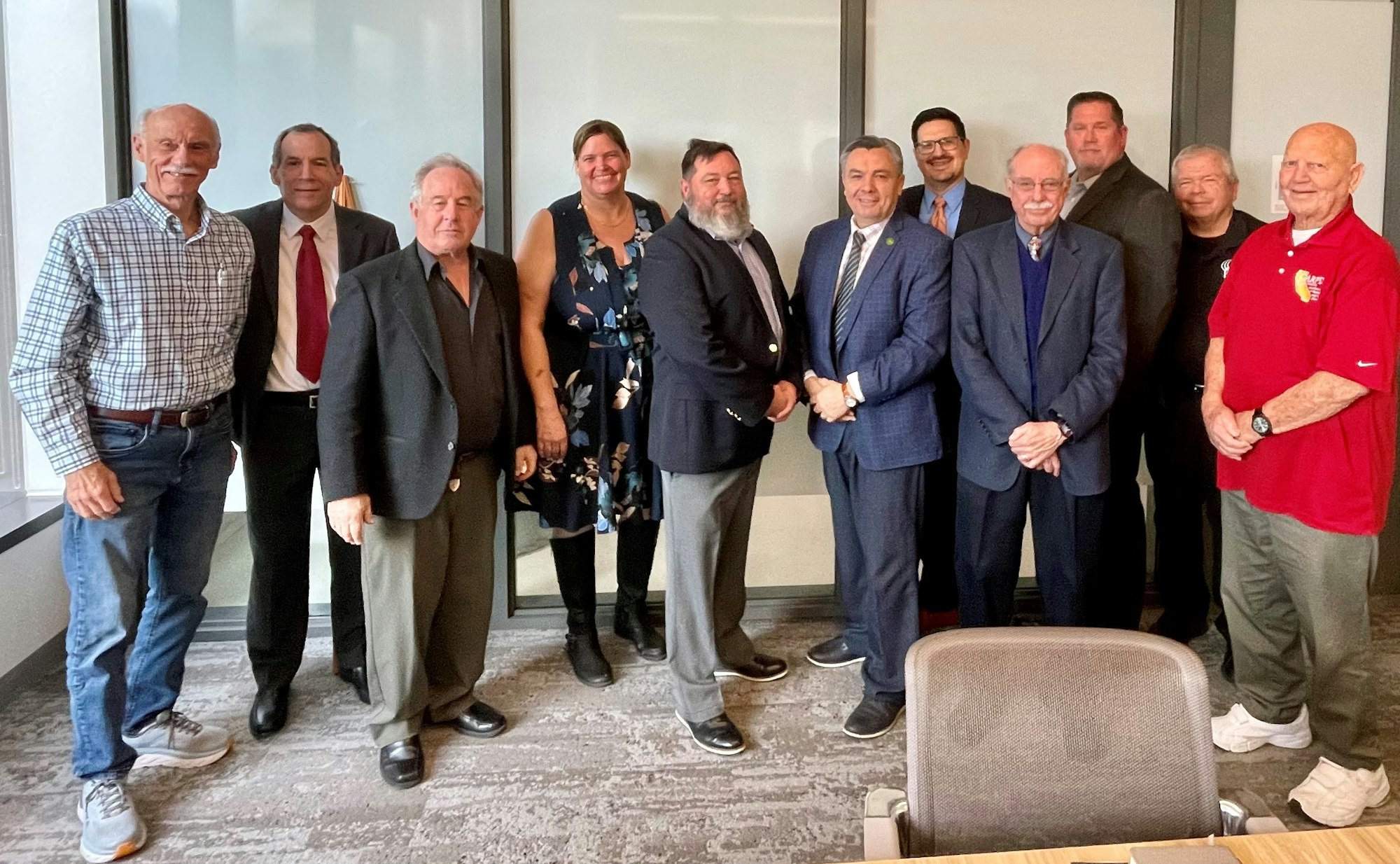 A group of 11 adults, mostly men, in business and casual attire, posing for a photo in an office-like setting.