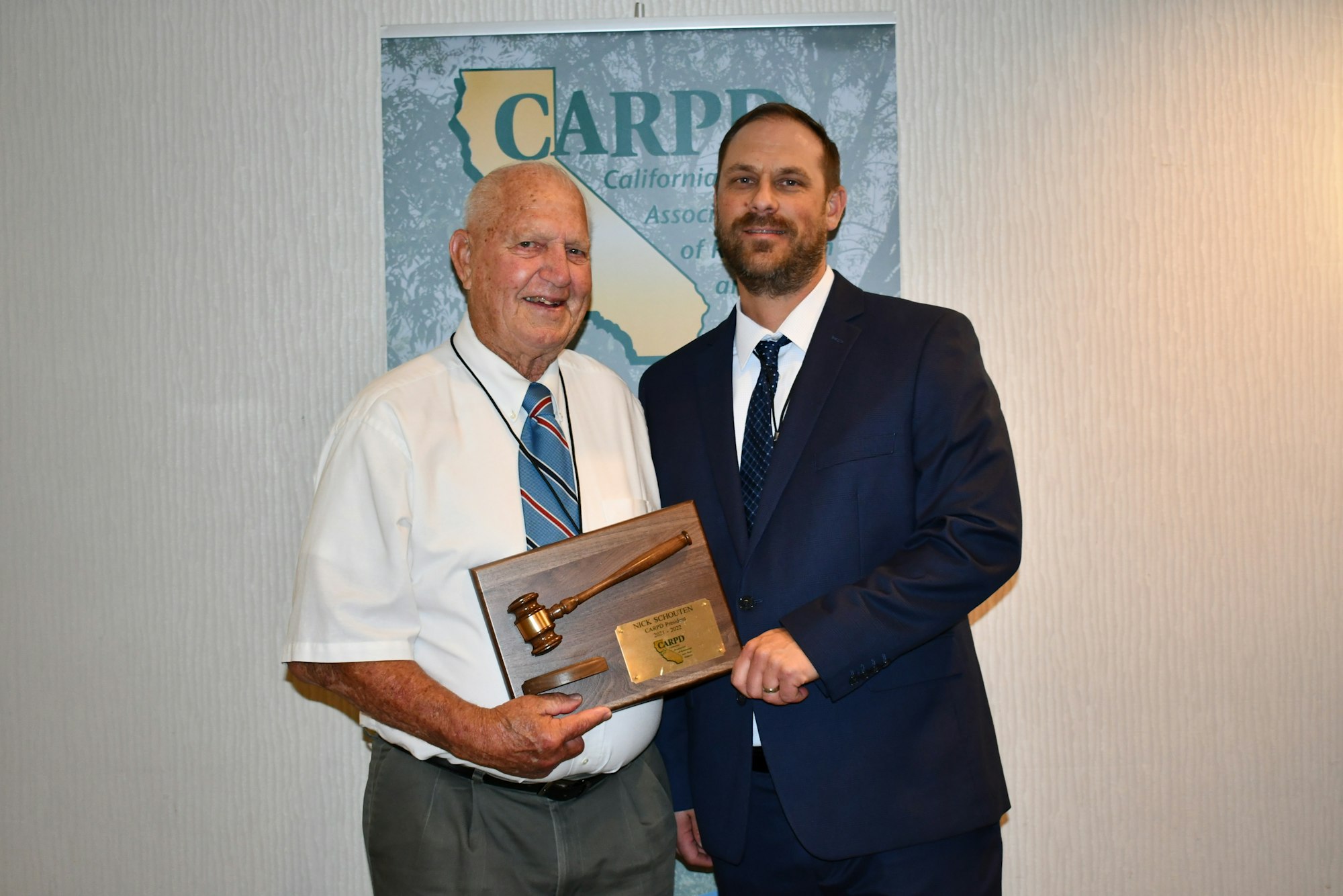 Two men pose for a photo, one holding a plaque with a gavel, at a California Association event.