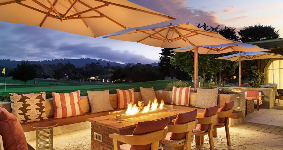 A cozy outdoor seating area with cushions and a fire pit overlooking a golf course at sunset.