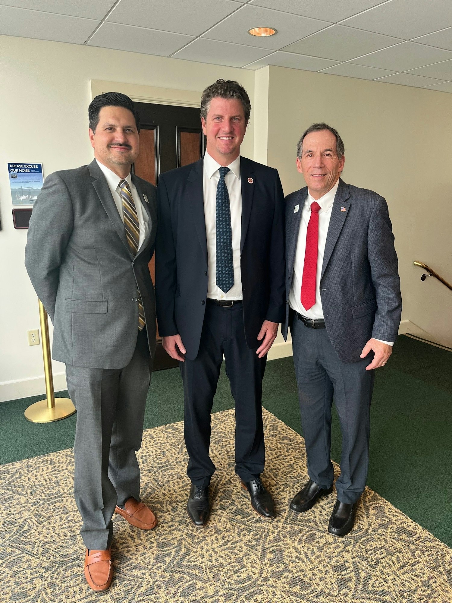 Three men in suits standing together in an indoor setting.
