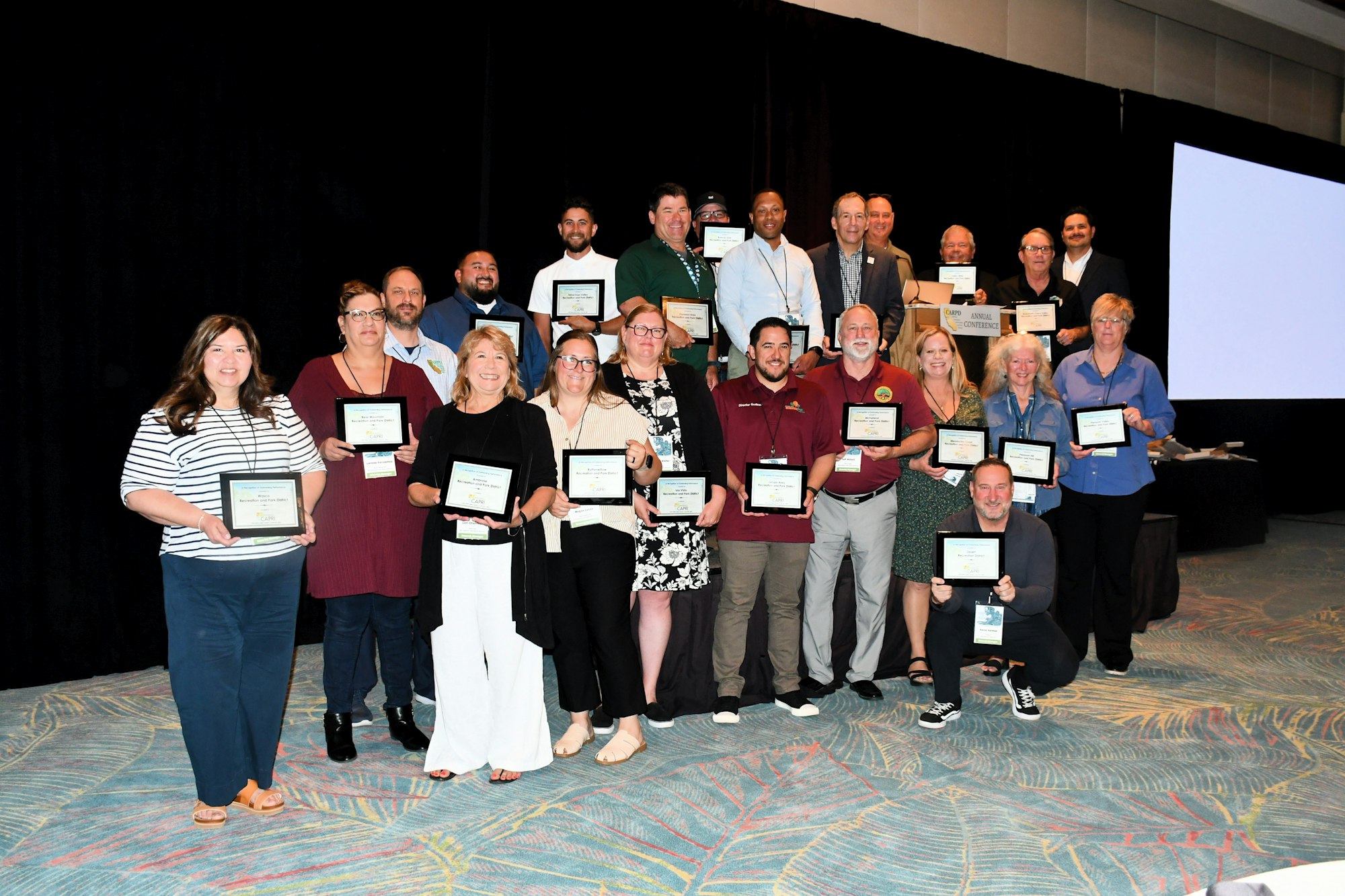 A group of people holding certificates, posing for a photo at an event or conference against a black background.