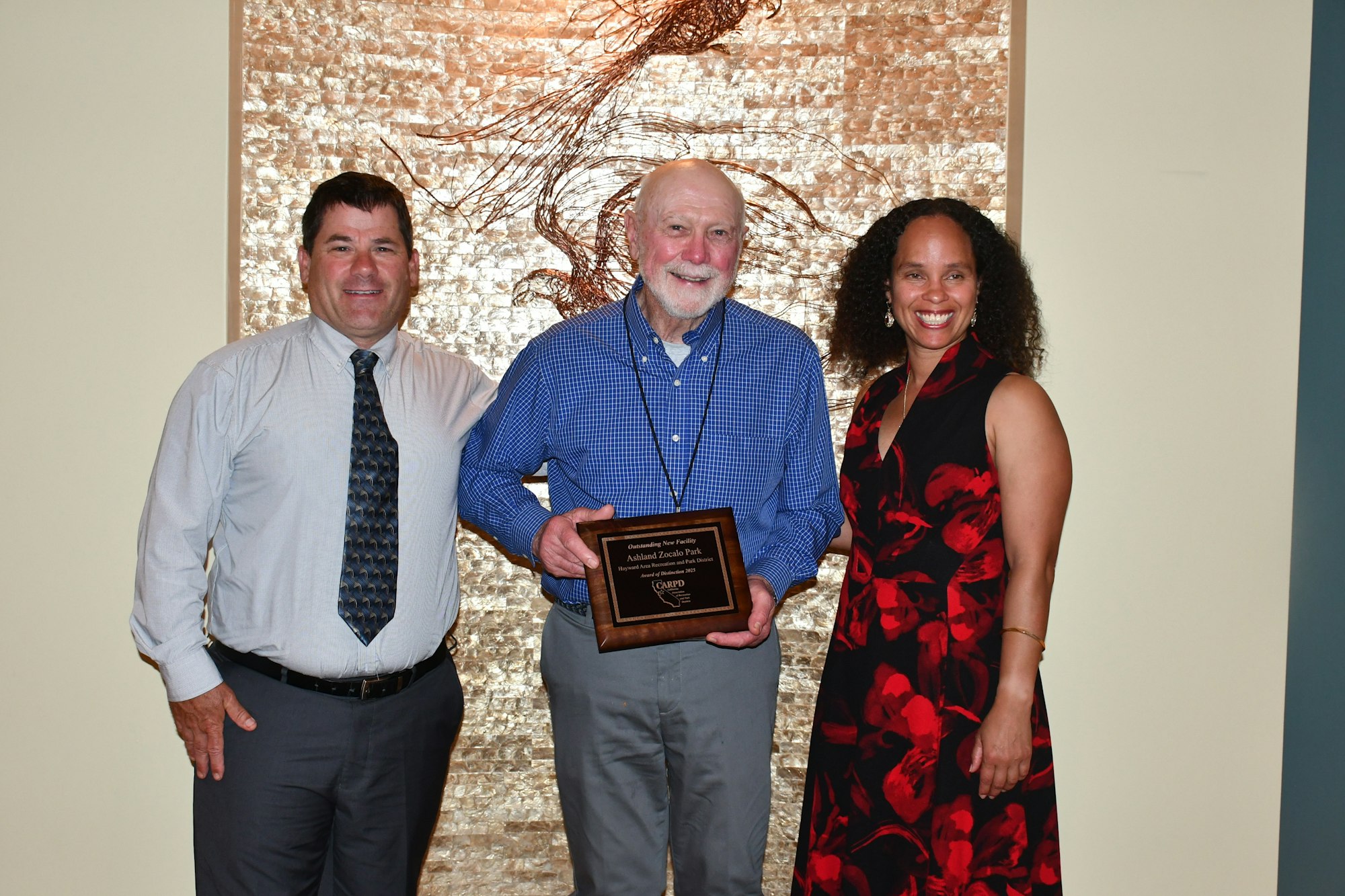 Three people posing, one holds a plaque.
