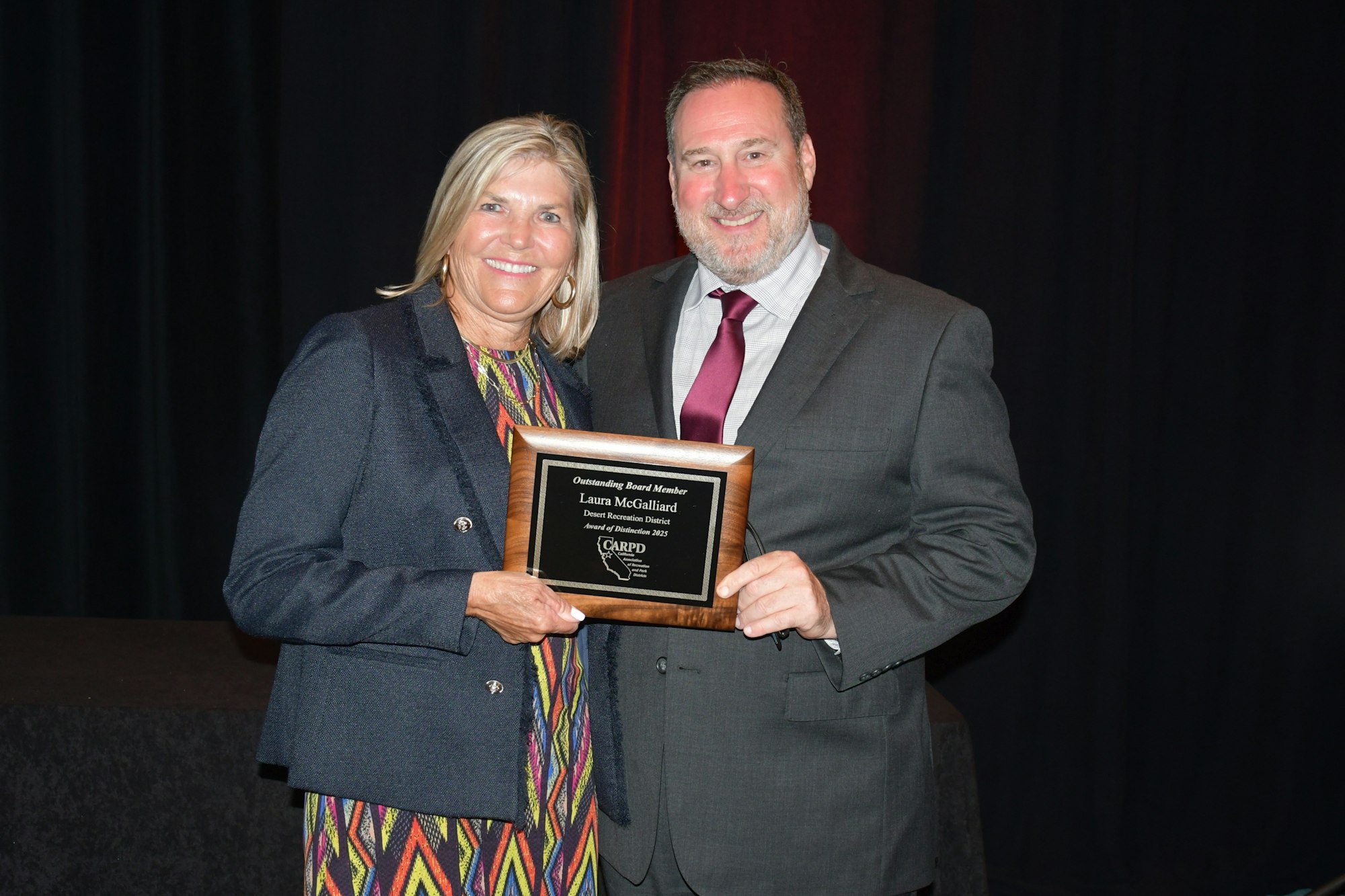 Two people smiling, one holding an award plaque.