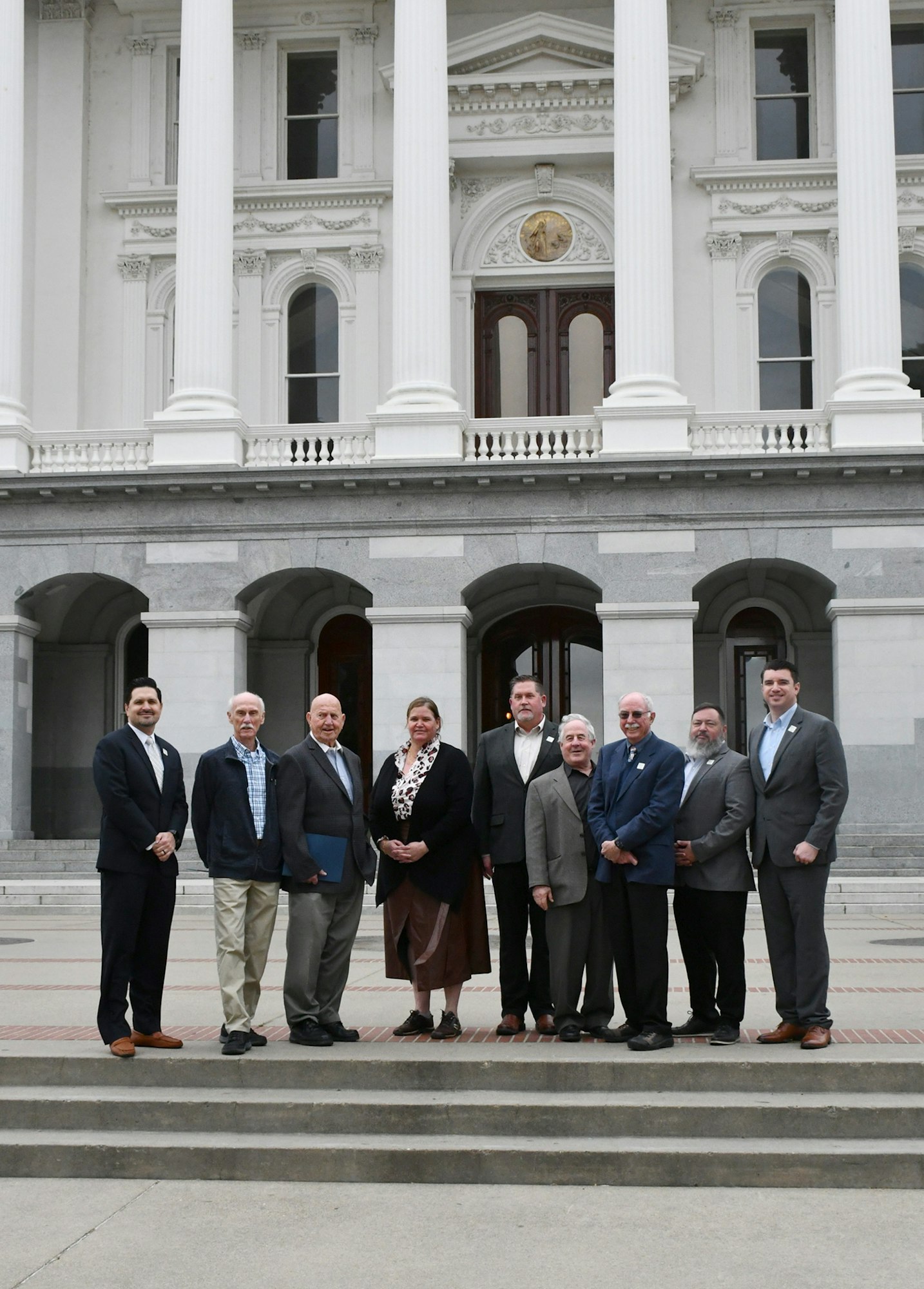 A group of people standing on steps in front of a classical building with large columns.