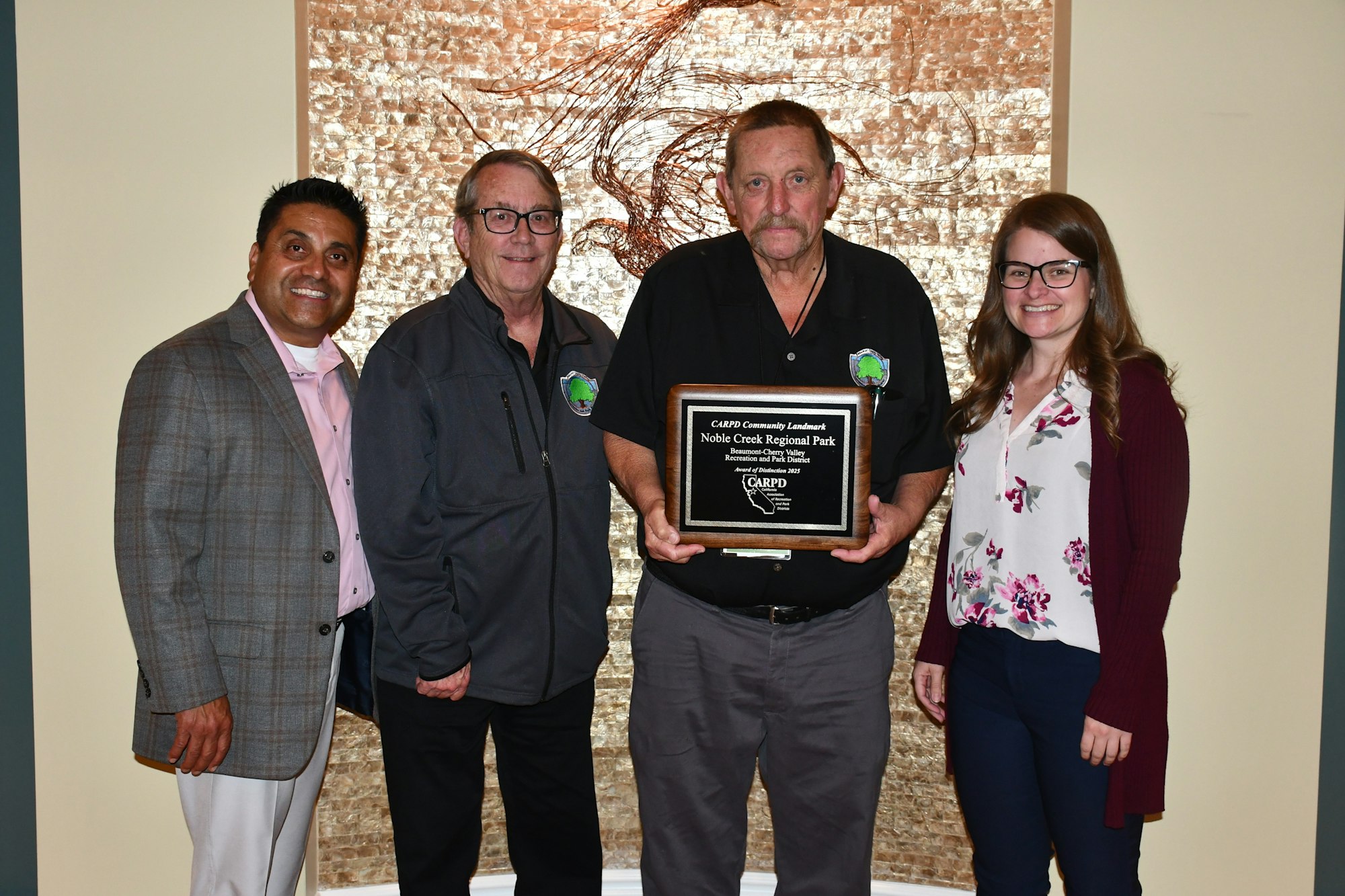 Four people posing with an award plaque for Noble Creek Regional Park in front of a textured background.