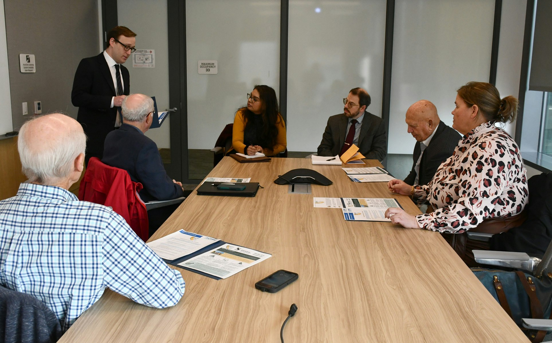 Seven people are in a conference room having a meeting, with documents on the table.