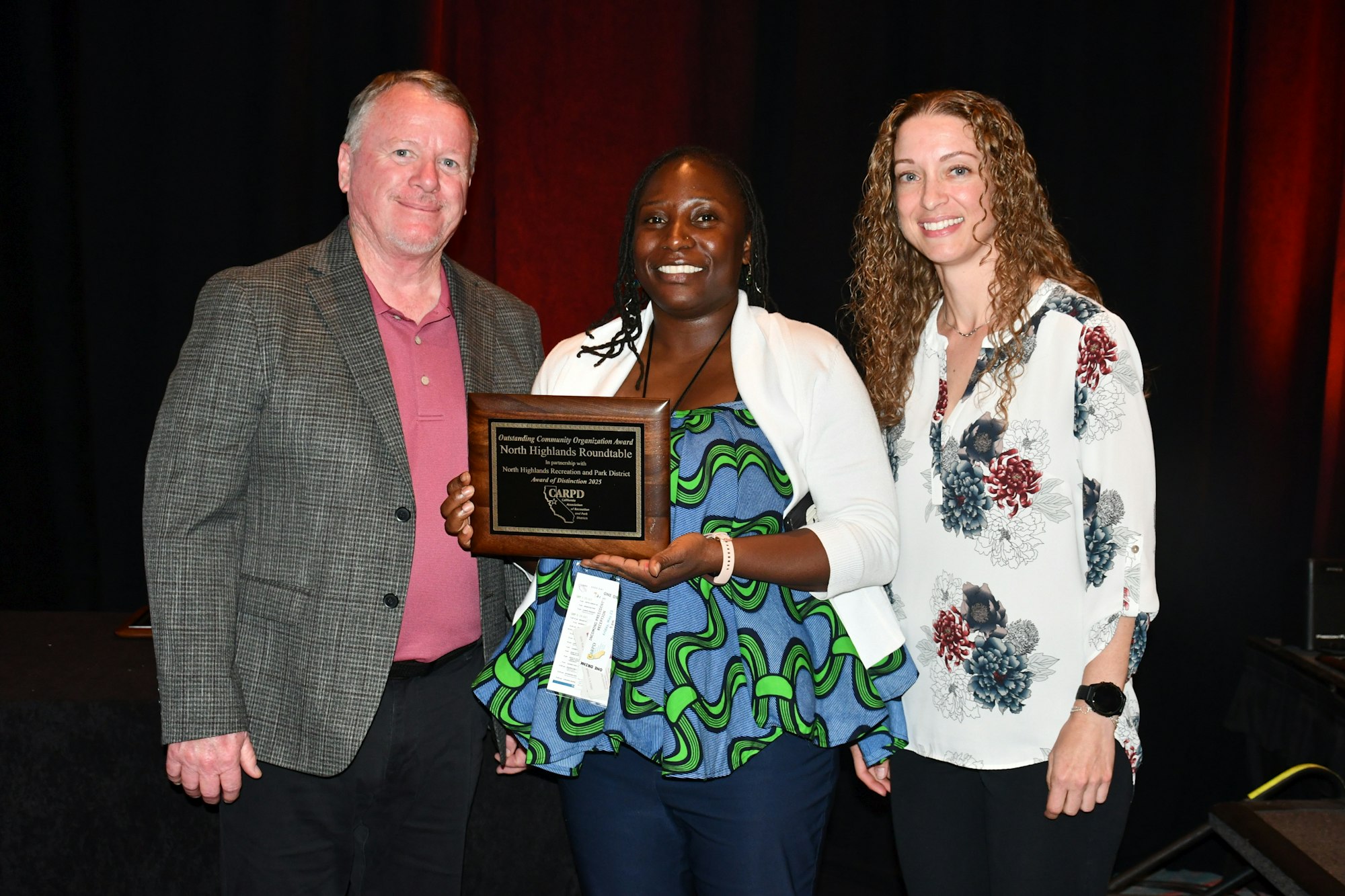 Three people pose with an award plaque, smiling.