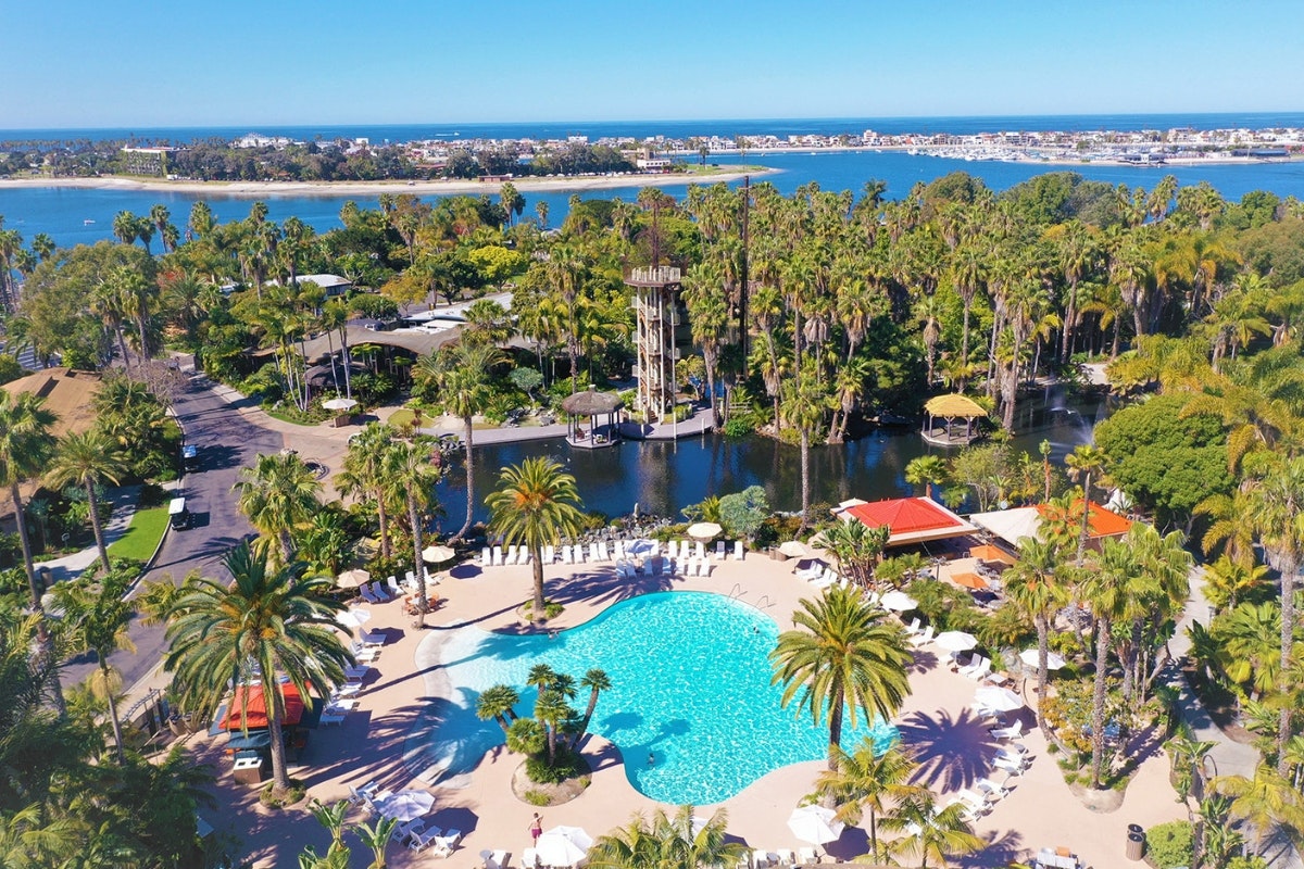 Aerial view of a tropical resort with a pool, palm trees, and a water tower near a coastline.
