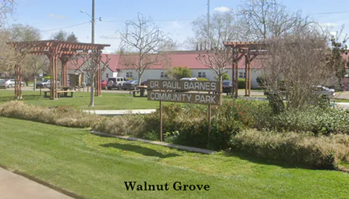 The image shows a park sign for Dr. Paul Barnes Community Park in Walnut Grove, with grassy areas and benches.