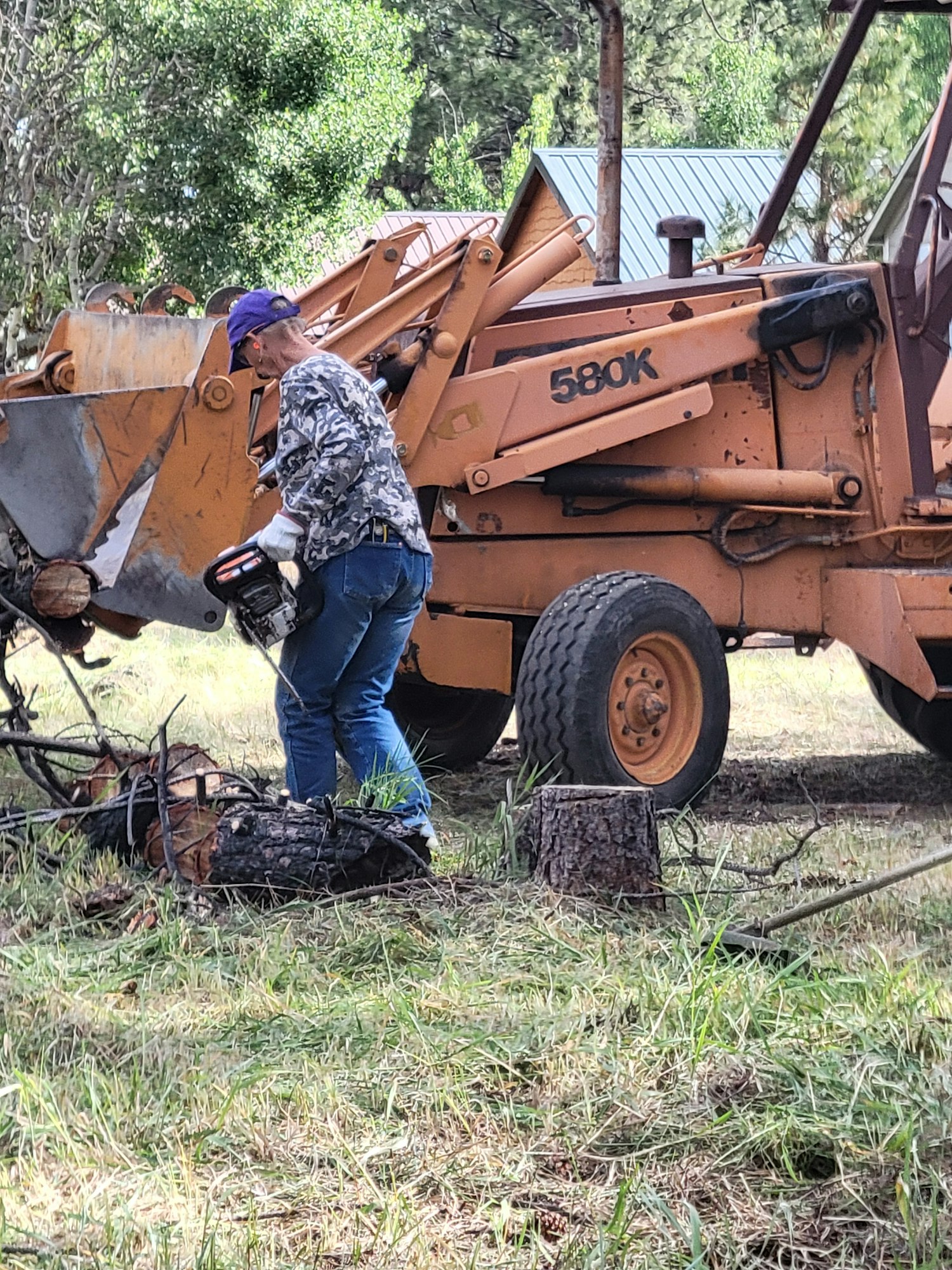 A person working on an overturned orange backhoe in a grassy area.