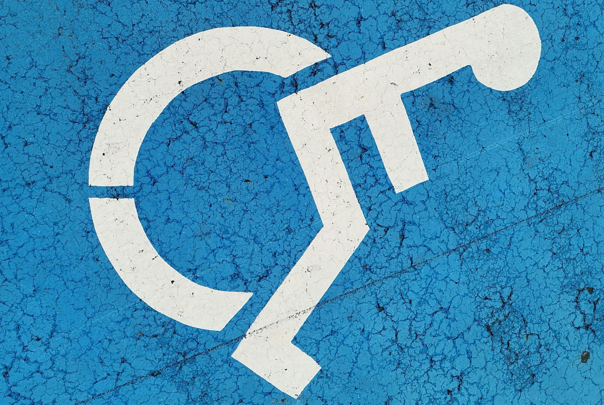 A cracked blue surface with a white wheelchair symbol, indicating parking for disabled persons.