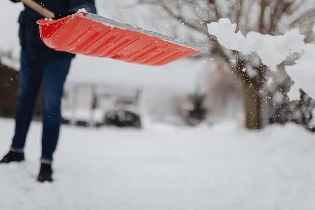 red snow shovel with someone shoveling snow