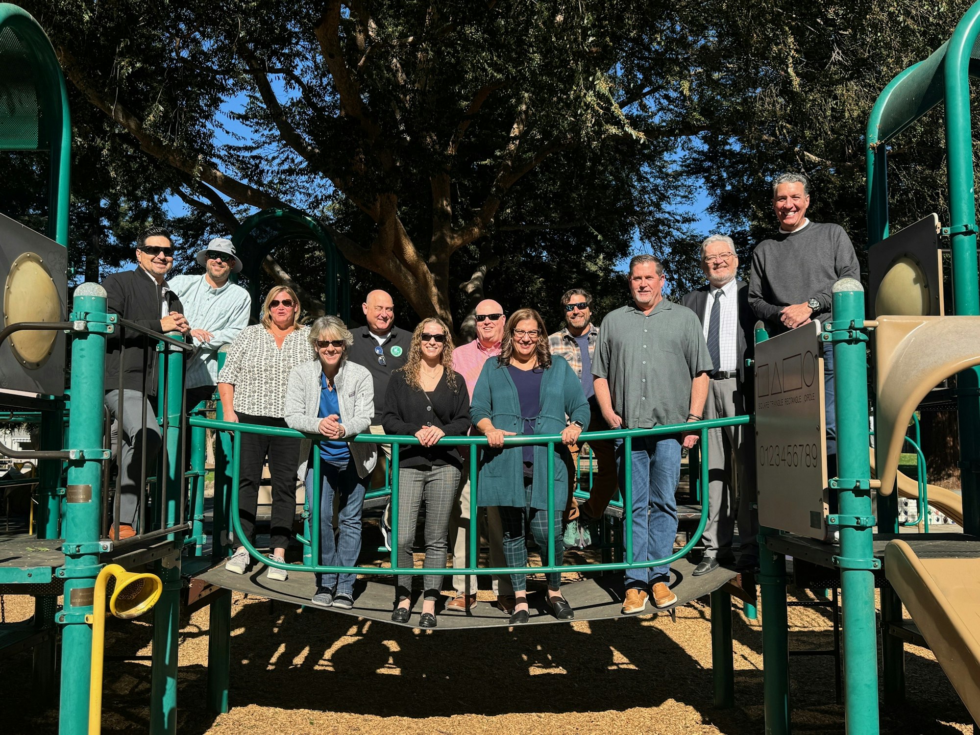 A group of people standing on a playground structure in a park on a sunny day.