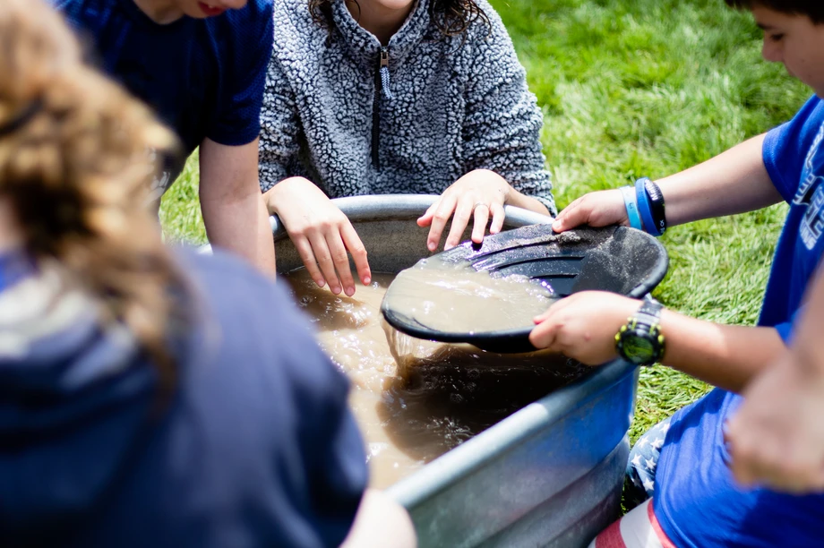 Children are panning for gems in a tub of water using sieves.