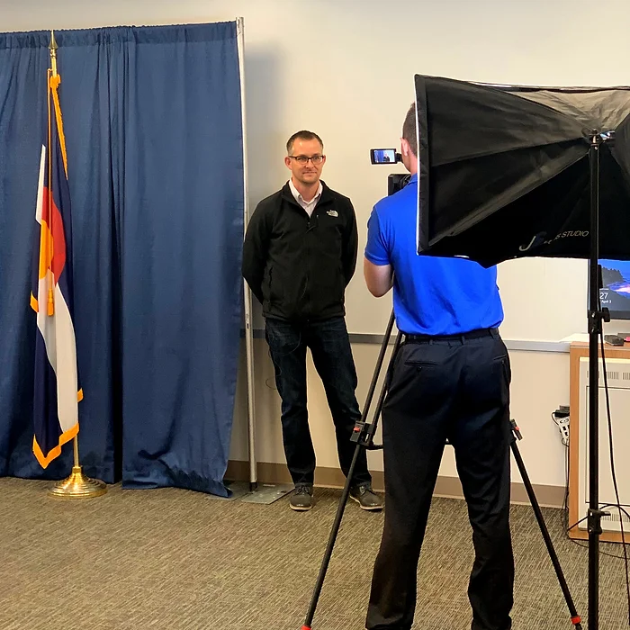 A person taking a photo of another person in a room with a flag.