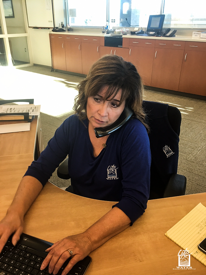 A person multitasking at a desk with a phone on their shoulder, working on a computer, in an office setting.