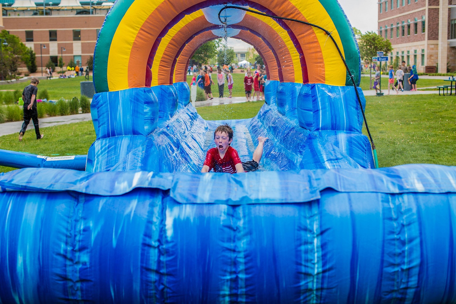 A child sliding down a colorful inflatable water slide with people in the background.