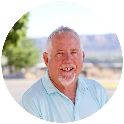 The image features a smiling older man with gray hair, dressed in a light blue shirt, set against a natural background.