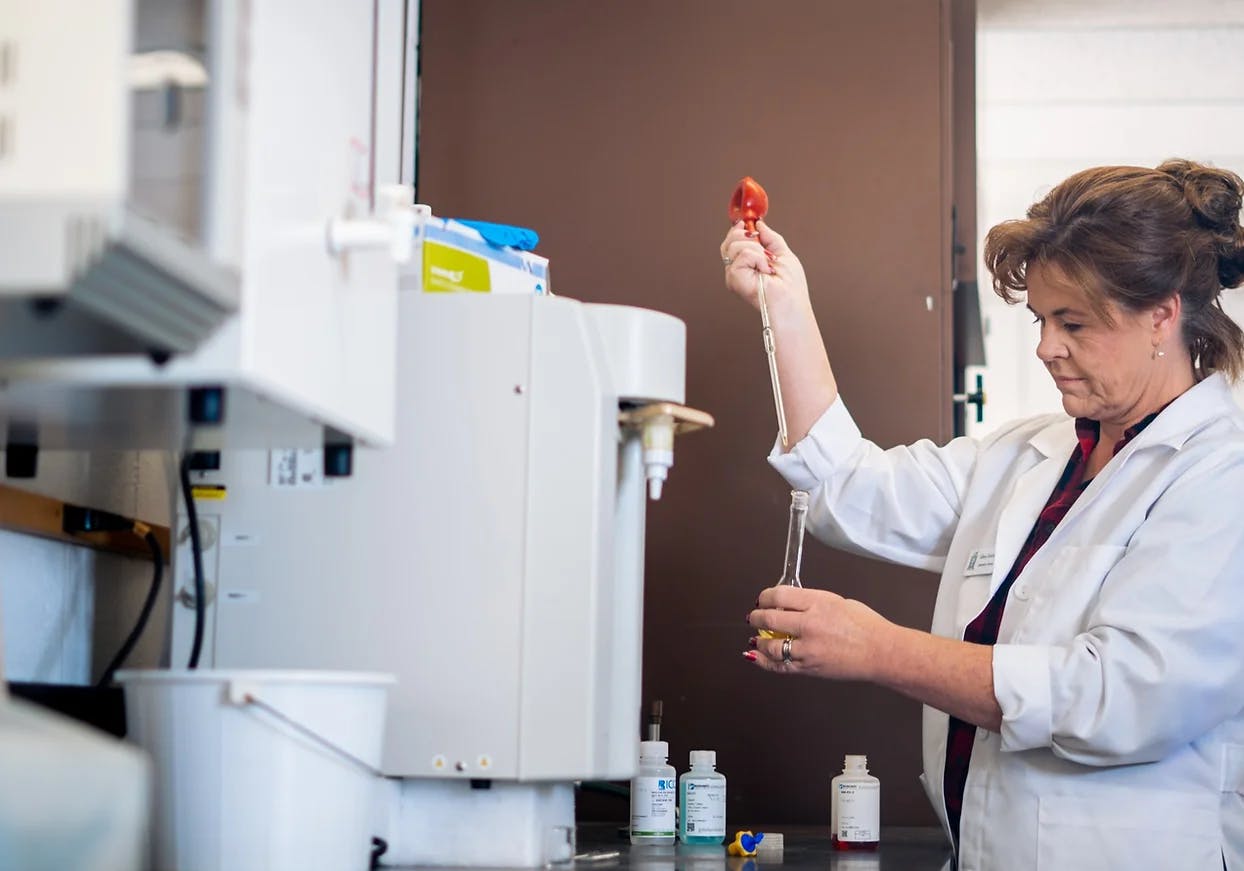 A scientist with a pipette and flask in a lab.