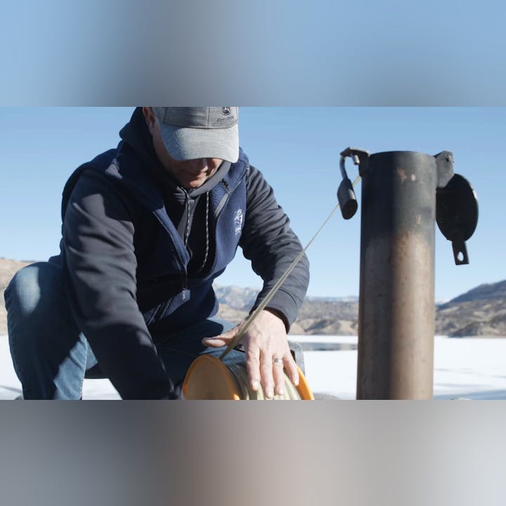 A person measuring ice thickness with an auger on a frozen surface.