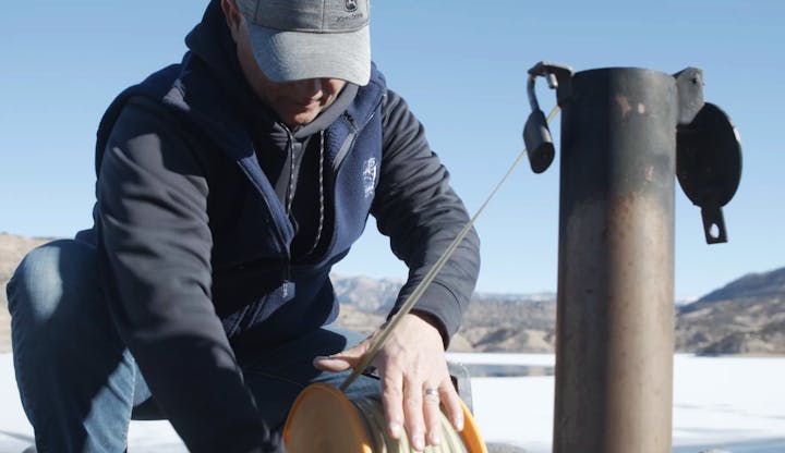A person measuring ice thickness with an auger on a frozen surface.