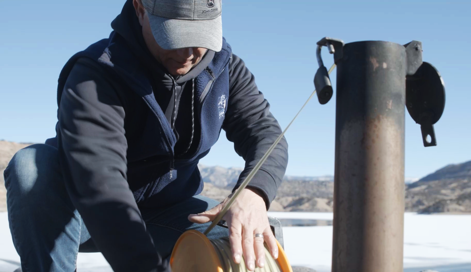 A person measuring ice thickness with an auger on a frozen surface.