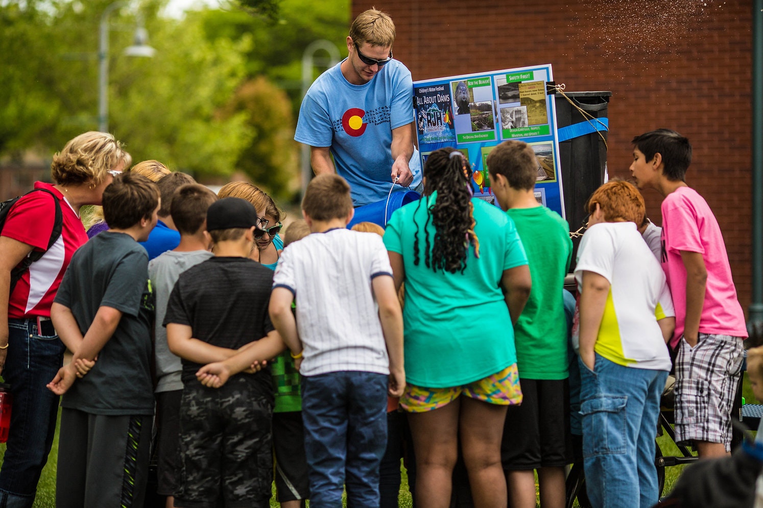 A group of children surrounds an adult at an outdoor educational exhibit.
