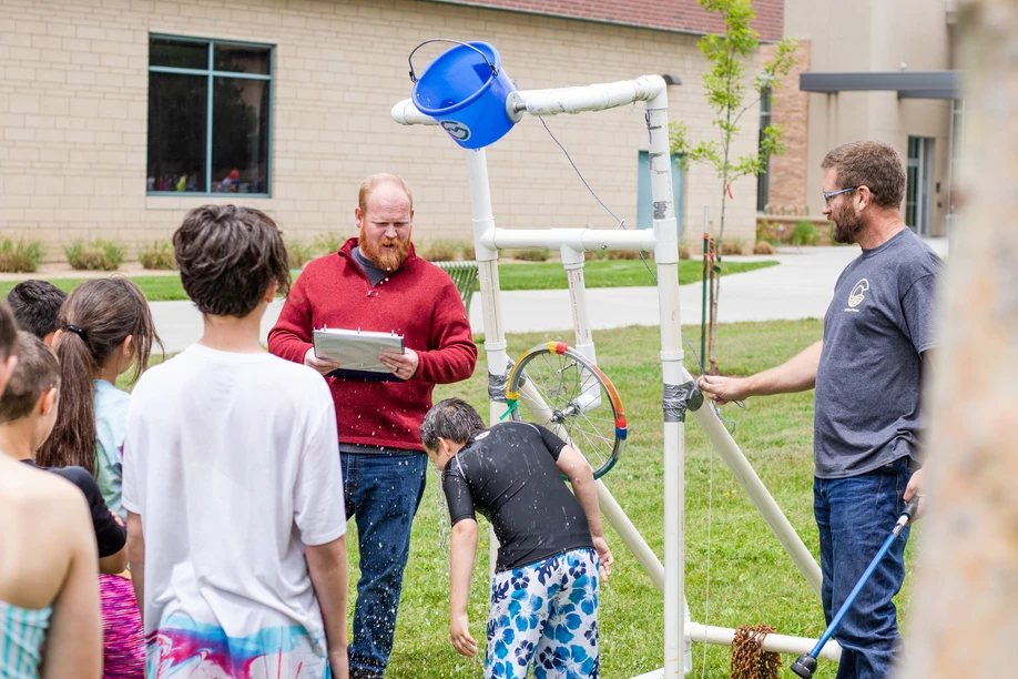 Group of people around a makeshift water dunk contraption outdoors.